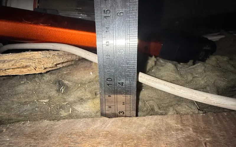 EPC assessor checking loft insulation depth with a ruler during a thorough assessment rather than a cheap EPC visit